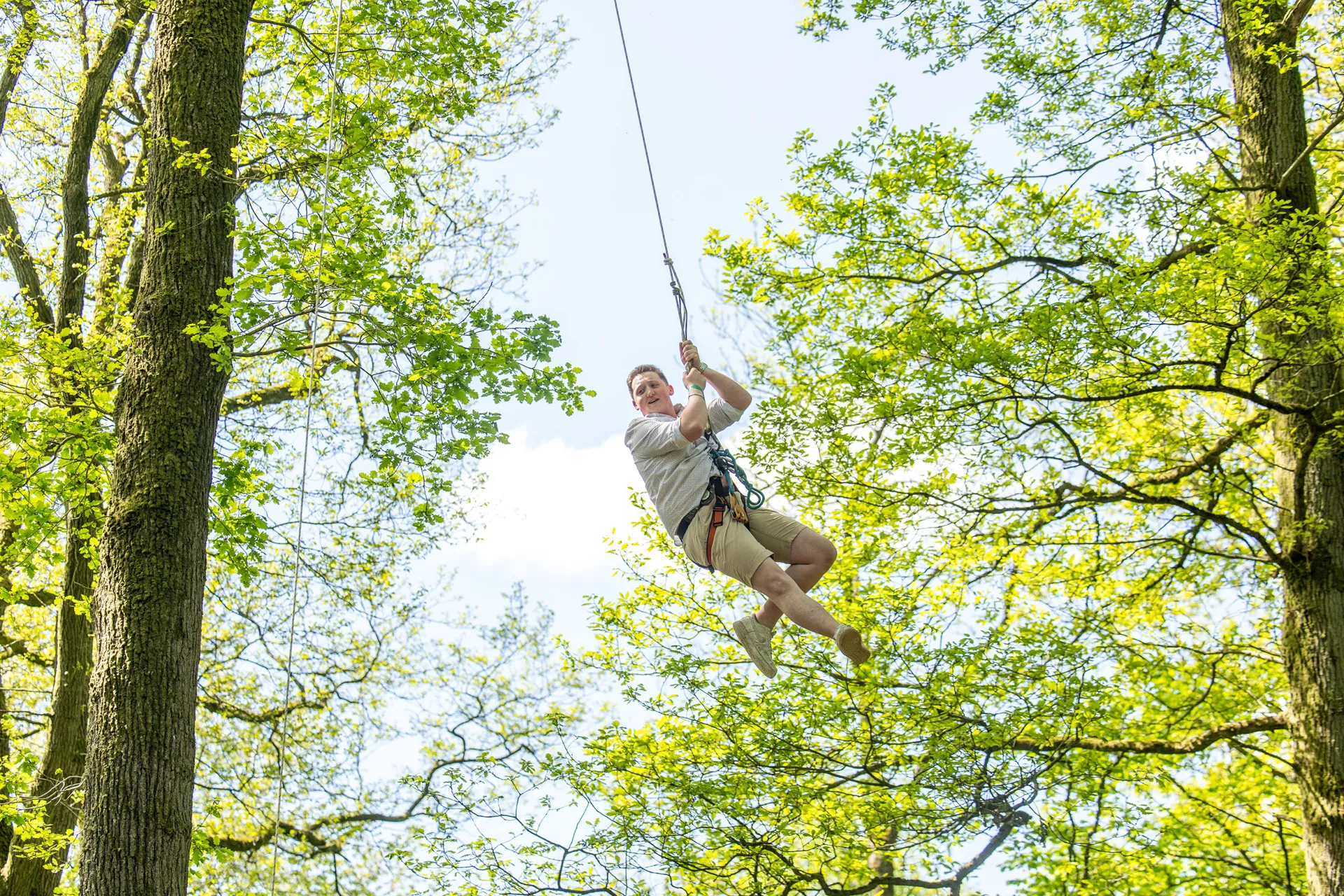 Un homme en train de glisser sur une tyrolienne en pleine forêt, avec des arbres verts en arrière-plan.